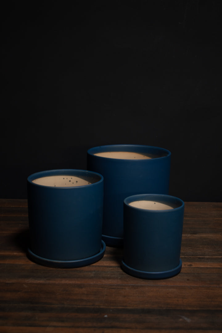 Three matte dark blue plant pots arranged on a rustic dark wooden surface against a solid black background.